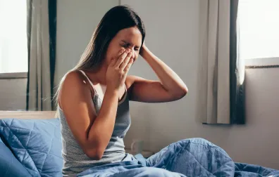 Vrouw zit op bed met handen op hoofd